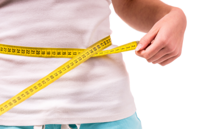 Woman wrapping measuring tape around chest, looking down at