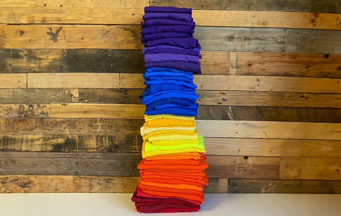 Red, orange, yellow, blue and purple t-shirts from ShirtSpace, folded and stacked high.